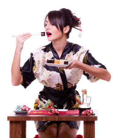 Young woman in Japanese kimono with chopsticks and sushi roll, isolated on white background.の写真素材
