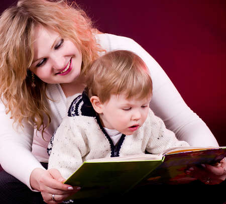 Mother and baby boy reading book and smiling  on red backgroundの写真素材