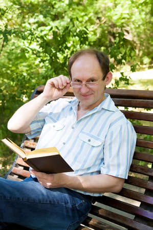 Happy aged man with glasses reading book in parkの写真素材
