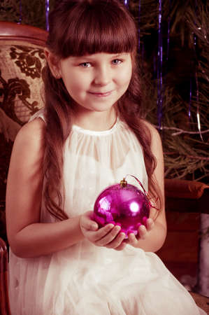 Beautiful little girl in white dress with Christmas tree decorationの写真素材