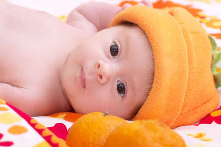 Newborn baby girl in orange hat with mandarin