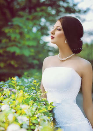 Beautiful bride with stylish make-up in white dress in spring garden