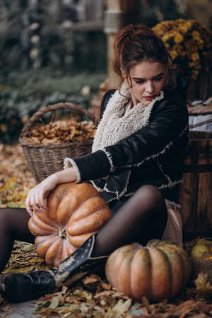 Beautiful girl in autumn garden with yellow flowers and pumpkinsの写真素材