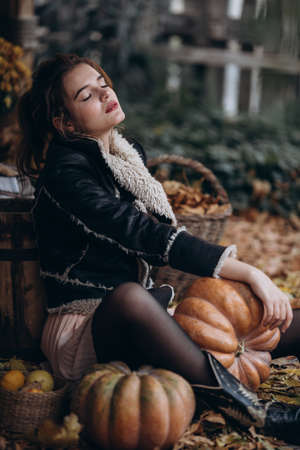 Beautiful girl in autumn garden with yellow flowers and pumpkinsの写真素材