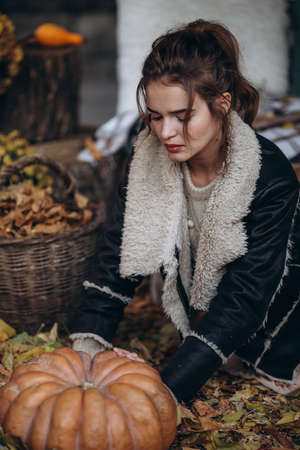 Beautiful girl in autumn garden with yellow flowers and pumpkinsの写真素材