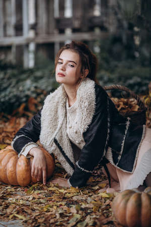 Beautiful girl in autumn garden with yellow flowers and pumpkinsの写真素材