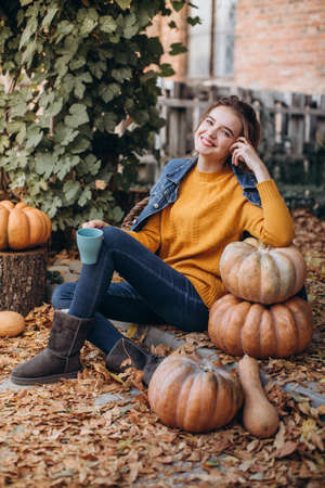 Beautiful girl in autumn garden with yellow flowers and pumpkinsの写真素材