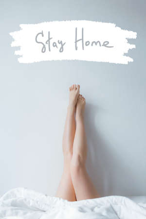 Stock photo - I stay at home awareness social media campaign and coronavirus prevention. Stay home phrase. Long female legs under the coversの写真素材