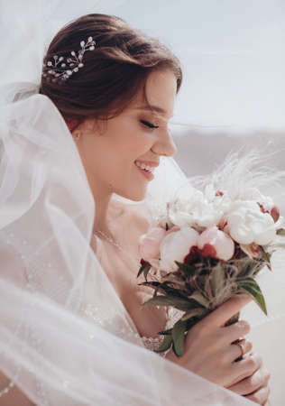 Beautiful brunette bride with stylish make-up in white dress with wedding bouquetの写真素材
