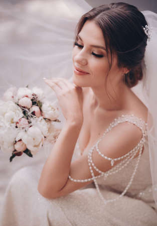 Beautiful brunette bride with stylish make-up in white dress with wedding bouquetの写真素材