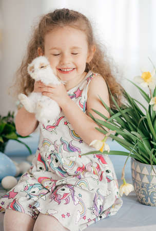 Stock Photo - Little girl play with rabbit indoors in spring. Decorated home and spring flowers. Family celebrating Easterの写真素材