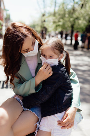 A woman and a little daughter in medical masks walk on the street during the  pandemic.