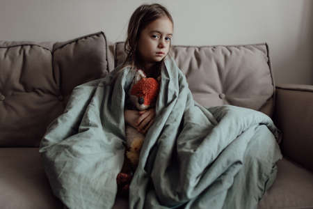 Ukrainian frightened child under a blanket. The girl is afraid of the sounds of air raids and...