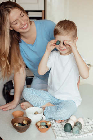 Happy family preparing Easter eggs indoors. Mother and boy celebrating happy Easter holiday together...