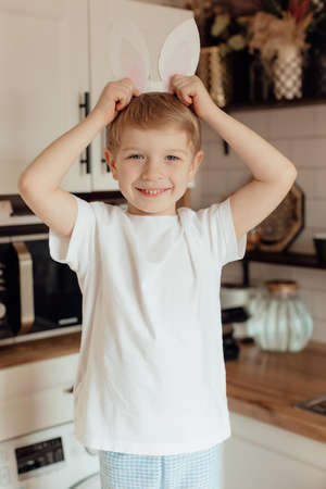 Happy boy with bunny ears made of cardboard and boy celebrating happy Easter holiday at home....