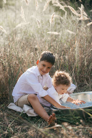 Happy two brothers are playing with water in a basin on wheat summer field. Adventure, travel, tourism, hike and people concept - happy family walkingの写真素材