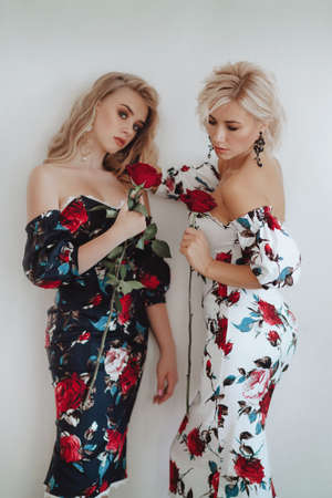 Beautiful young mother and her teenage daughter in identical dresses with roses on a light background. Happy motherhood. Teen parenting conceptの写真素材