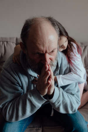 Ukrainian worried middle aged hoary man supporting little frightened grandgirl. Unhappy mature older grandfather with little girl at home. concept of stress and fearの写真素材