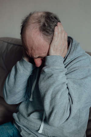 Ukrainian worried middle aged man was frightened by the loud sound and closed his ears in fear. Unhappy mature older grandfather at home.の写真素材