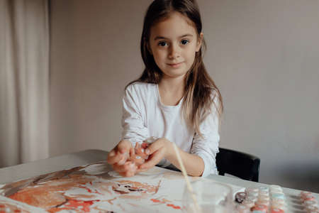 Happy preschooler girl paints a picture by numbers with a brush and gouache. Home entertainment and hobbies conceptの写真素材