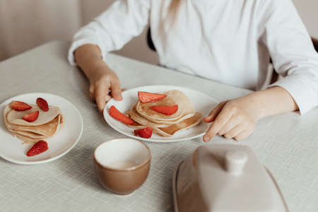 Hungry little girl eat sweet panckaces with strawberries. Family breakfast concept
