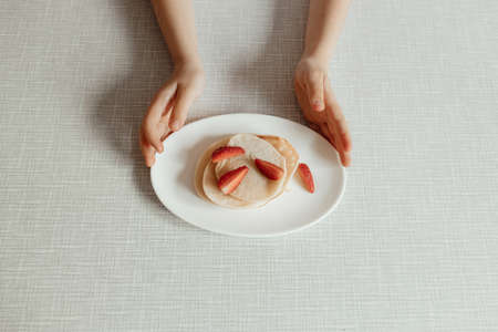 Hungry little girl eat sweet panckaces with strawberries. Family breakfast conceptの写真素材