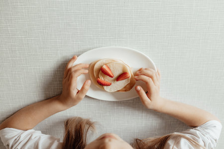 Hungry little girl eat sweet panckaces with strawberries. Family breakfast conceptの写真素材