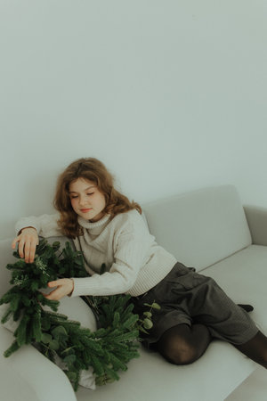 Beautiful festive portrait of a teen girl. Christmas light home background. Waiting for a miracle make a wish under the Christmas tree. Charming smile. New Year's holiday atmosphereの写真素材