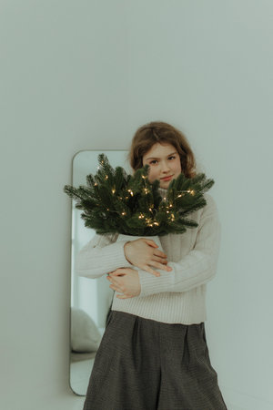Beautiful festive portrait of a teen girl. Christmas light home background. Waiting for a miracle make a wish under the Christmas tree. Charming smile. New Year's holiday atmosphereの写真素材
