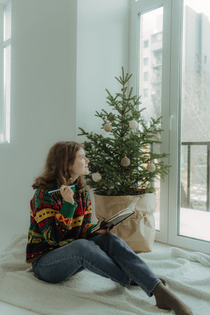 Beautiful festive portrait of a teen girl. Christmas light home background. Waiting for a miracle make a wish under the Christmas tree. Charming smile. New Year's holiday atmosphereの写真素材