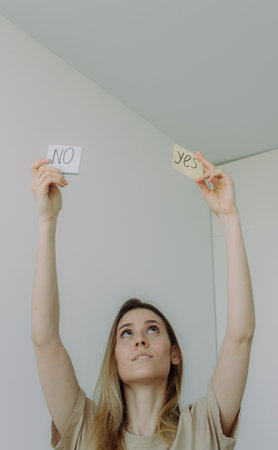 Young beautiful blonde woman with a sign Yes and No. Choice and question answer concept, the choice...