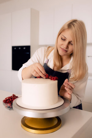 Pastry chef confectioner young caucasian woman in the kitchen. She decorating cake.