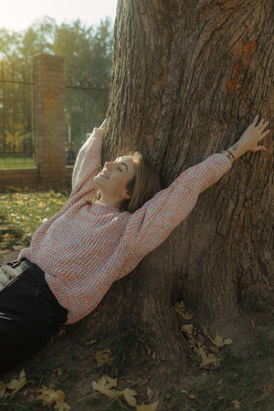 Woman with happy smile on face in park, rejoices. Girl in casual demi-season clothes on blurred background of city parkの写真素材
