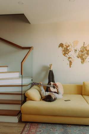 Creative hobby. Talented young female musician sit in armchair alone compose instrumental song using classic guitar. Smiling lady play calm melody on musical instrument. Copy spaceの写真素材
