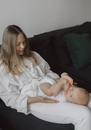Side view of a young woman playing with her little baby in bed. The concept of happy motherhood and newborn careの写真素材