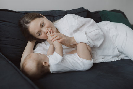 Side view of a young woman playing with her little baby in bed. The concept of happy motherhood and...