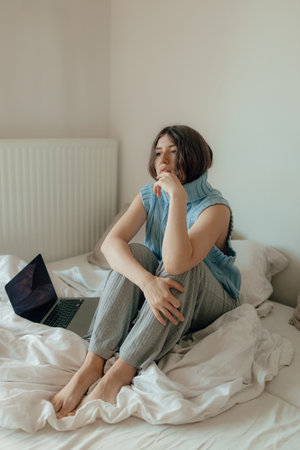 Young woman posing in the bedroom, have fresh glow make up, laptop sitting at home write messages. Photo concept with soft focus and noises. Technology and content marketing concept.の写真素材