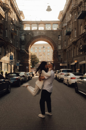 The couple walks around Kyiv. Old city. Love story. Walk around the city. A woman in a white suit. Guy in a t-shirt and jeans. Love and hugs. To cross the road. No focus blurred and noise effect.の写真素材
