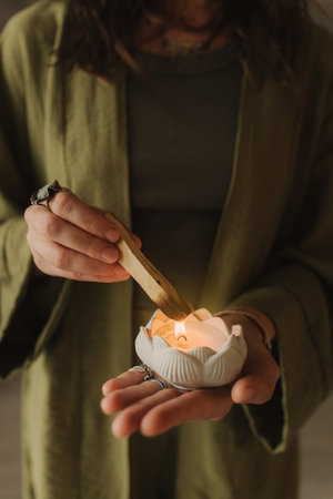 A young woman holds a smoking palo santo stick in her hands. Buddhist healing practices.Clearing the space of negative energy. Aromatherapy. Selective focus,close up. Soft focus and noise effect.の写真素材