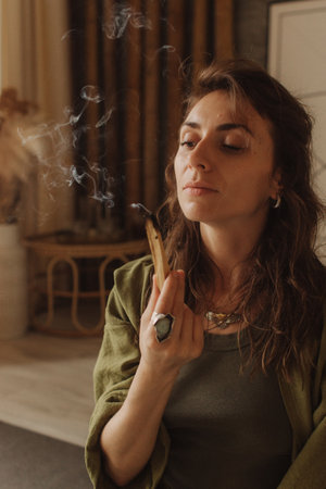 A young woman holds a smoking palo santo stick in her hands. Buddhist healing practices.Clearing the space of negative energy. Aromatherapy. Selective focus,close up. Soft focus and noise effect.の写真素材