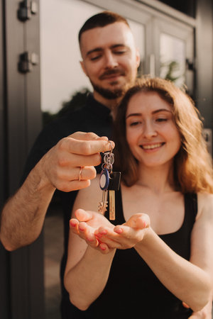 Focus on keys, held by excited young spouses homeowners. Happy married family couple celebrating moving in new house home , demonstrating keys, standing in apartment, real estate mortgage concept.の写真素材