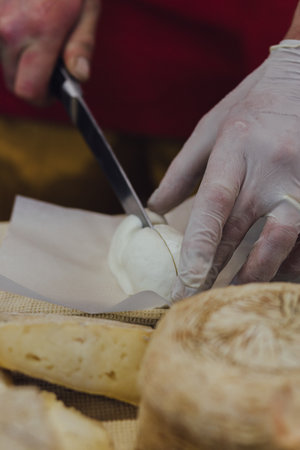Cheesemaker cuts cheese. Pieces of cheese on a wooden board with cook hands and a knife. Cutting...