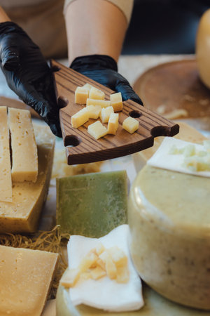 Cheesemaker cuts cheese. Pieces of cheese on a wooden board with cook hands and a knife. Cutting...