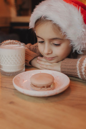 Cute little girl in Santa hat with delicious Christmas cookie and milk at home. Xmas home holiday celebration.の写真素材