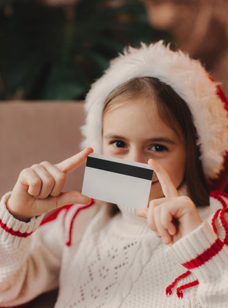 A school-age girl wearing a red Santa hat does Christmas shopping online  . New Year's online shopping.の写真素材