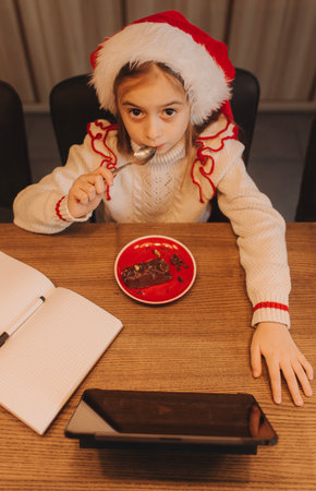 Happy girl enjoys the Christmas holidays, eating a chocolate dessert while looking at a tablet iPad in a cafe.の写真素材