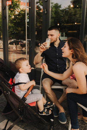 Happy young family with baby son eating lunch together at restaurant and having fun. Soft focus blurred and noise effect.の写真素材