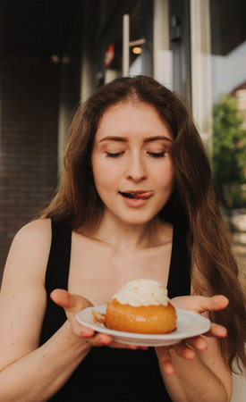 Portrait of a satisfied woman eating a cake while sitting at the table in a cafe indoors. Closeup of girl eating in a cafe. Selective focus, noise effect. Unhealthy eating concept.の写真素材