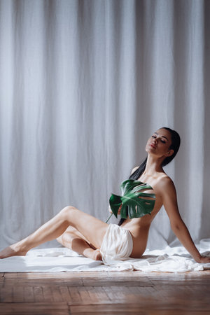 Portrait of beautiful young woman with slim figure covering her body with a cloth and green leaf . Self-love. Concept of beauty, style, fashion, cosmetology, body and skin care, sport, ad.の写真素材