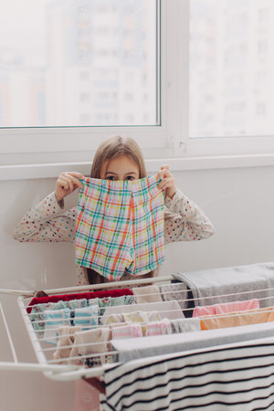 Teen girl in laundry room. Clean washed clothes on drying rack. Mother's little helper, little girl...